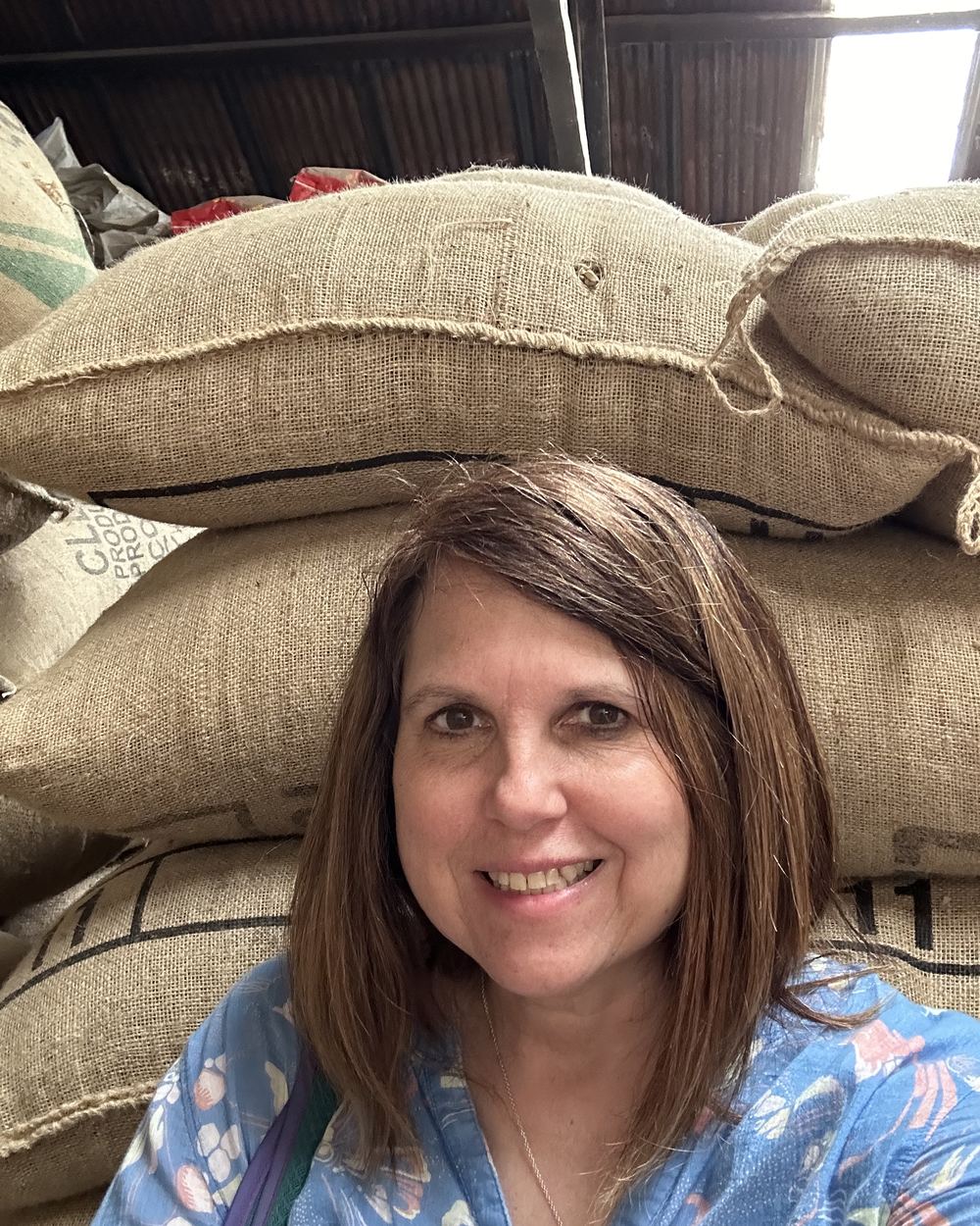 Jill Killen standing in front of stacked burlap sacks of green coffee at a warehouse
